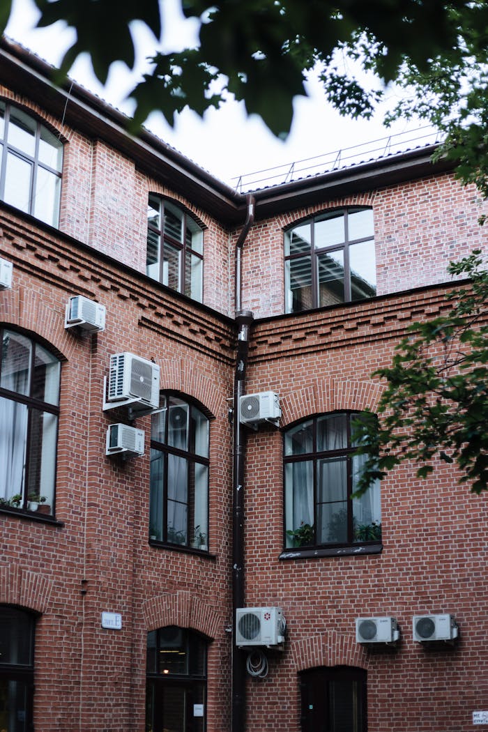 Red brick building exterior featuring multiple air conditioning units and large windows.